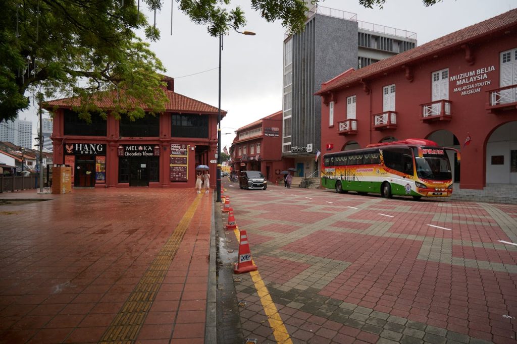 City street scene in Malacca featuring red brick buildings and a colorful bus on an overcast day.